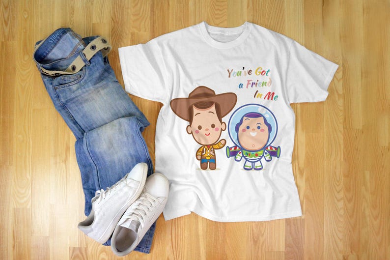 May include: White t-shirt with a cartoon image of Woody and Buzz Lightyear from Toy Story. The shirt has the text "You've Got a Friend in Me" printed on it.