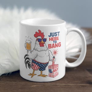 May include: White ceramic coffee mug with a red, white, and blue rooster wearing sunglasses and holding a beer. The mug has the text "Just Here To Bang" and a red, white, and blue firework with the text "July 4th".
