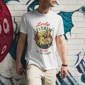 May include: White t-shirt with a cartoon image of Goofy fishing. The text "Lucky Fishin' Shirt Do Not Wash" is printed on the shirt.
