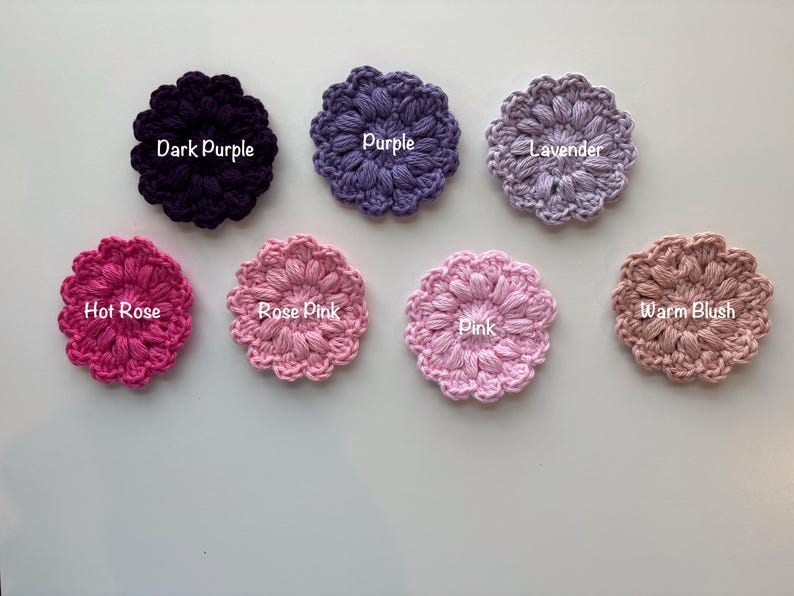 May include: Seven circular crochet flower appliques arranged in two rows. The top row features Dark Purple, Purple, and Lavender. The bottom row includes Hot Rose, Rose Pink, Pink, and Warm Blush. Each piece has a textured, puff-stitch design.