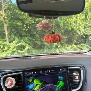 Puede incluir: Un conjunto de accesorios de coche tejidos a ganchillo que incluye un adorno colgante de calabaza y pastel para el espejo retrovisor, un clip de flor y un clip de bal&oacute;n de f&uacute;tbol para la ventilaci&oacute;n, en tonos naranja, marr&oacute;n, blanco y beige.