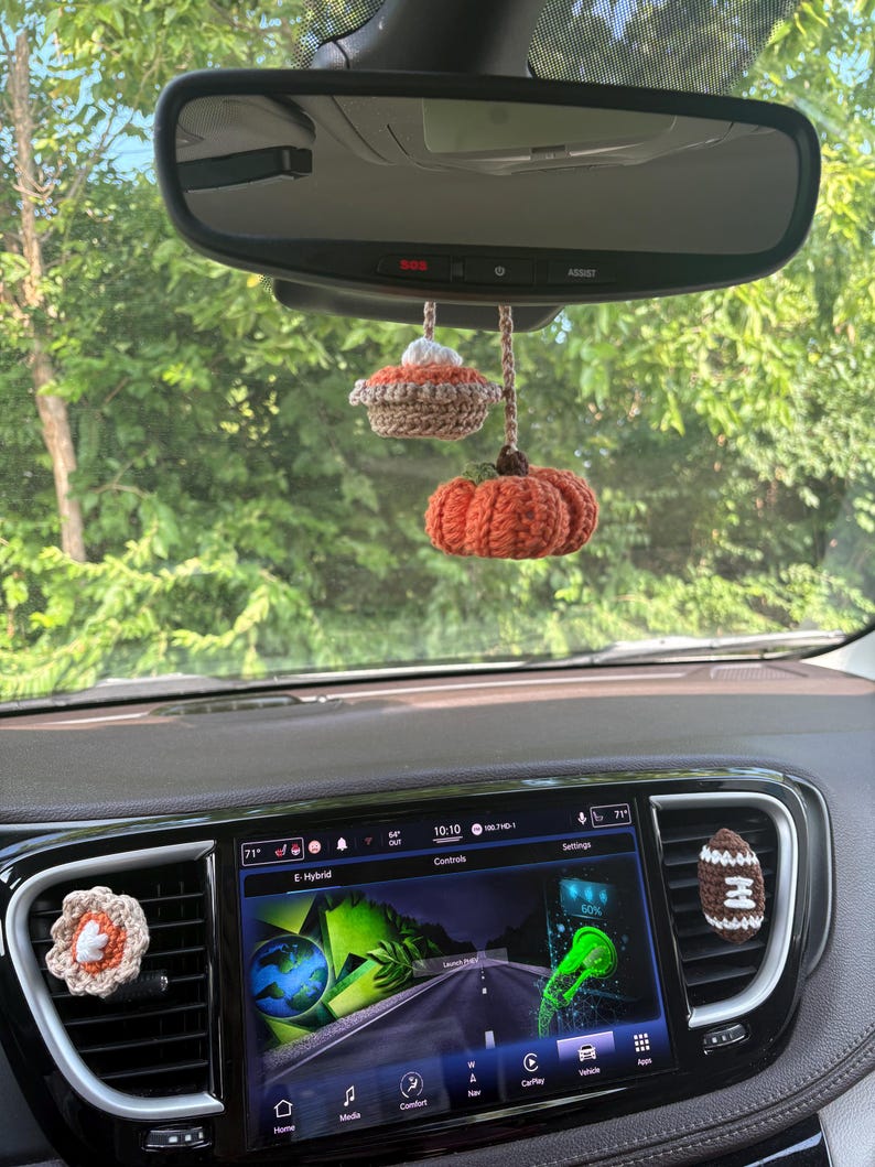 Puede incluir: Un conjunto de accesorios de coche tejidos a ganchillo que incluye un adorno colgante de calabaza y pastel para el espejo retrovisor, un clip de flor y un clip de bal&oacute;n de f&uacute;tbol para la ventilaci&oacute;n, en tonos naranja, marr&oacute;n, blanco y beige.