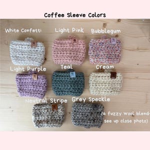 May include: Eight crocheted coffee sleeves in various colours including white confetti, light pink, bubblegum, light purple, teal, cream, neutral stripe, and grey speckle. Each sleeve features a small rectangular brand tag and a textured yarn finish.