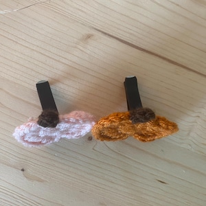 Puede incluir: Dos pinzas para el pelo con dise&ntilde;os de flores de ganchillo. Una pinza tiene una flor de ganchillo rosa claro con un centro marr&oacute;n oscuro, y la otra tiene una flor de ganchillo naranja con un centro marr&oacute;n oscuro. Ambas van sobre pinzas negras.