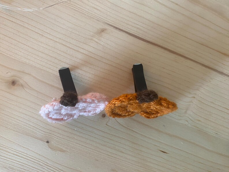 Puede incluir: Dos pinzas para el pelo con dise&ntilde;os de flores de ganchillo. Una pinza tiene una flor de ganchillo rosa claro con un centro marr&oacute;n oscuro, y la otra tiene una flor de ganchillo naranja con un centro marr&oacute;n oscuro. Ambas van sobre pinzas negras.