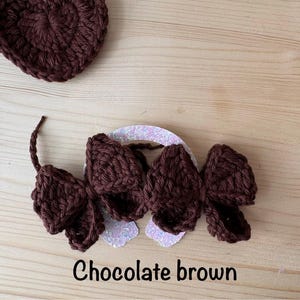 May include: A chocolate brown crochet heart and a matching hair accessory with three bow-shaped elements. The accessory is attached to a glittery white base. The text "Chocolate brown" is at the bottom.