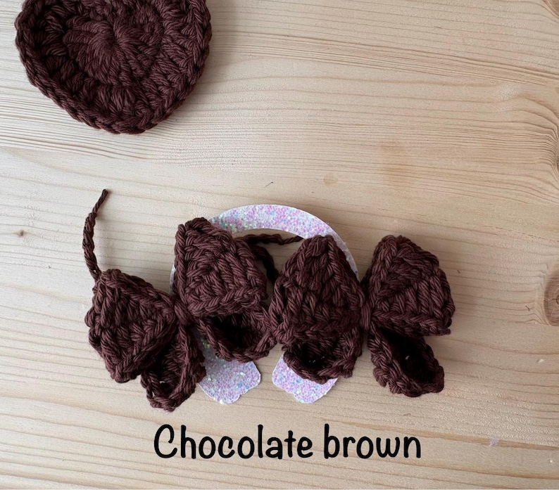 May include: A chocolate brown crochet heart and a matching hair accessory with three bow-shaped elements. The accessory is attached to a glittery white base. The text "Chocolate brown" is at the bottom.