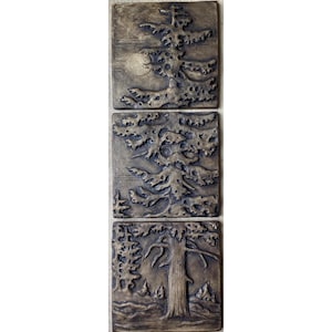 May include: A vertical arrangement of three square bronze-toned tiles featuring embossed relief designs of coniferous trees. Each tile displays a textured, dark metallic finish with raised details depicting tree branches and trunks.