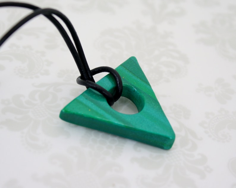 May include: A green triangle pendant with a hole in the center, hanging from a black cord.