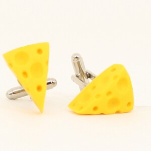 Puede incluir: Un par de gemelos en forma de queso amarillo. Los gemelos est&aacute;n hechos de metal y tienen un acabado plateado.