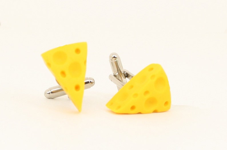 Puede incluir: Un par de gemelos en forma de queso amarillo. Los gemelos est&aacute;n hechos de metal y tienen un acabado plateado.
