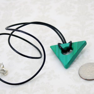 May include: A green triangle pendant with a hole in the center, hanging from a black leather cord. The pendant is about the size of a US quarter.