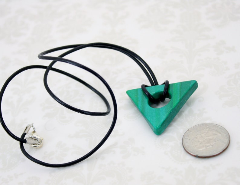 May include: A green triangle pendant with a hole in the center, hanging from a black leather cord. The pendant is about the size of a US quarter.