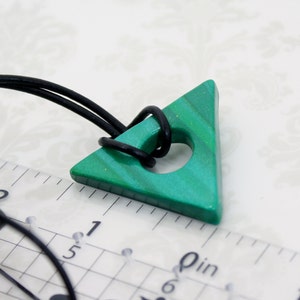 May include: A green triangle pendant with a hole in the center, hanging from a black cord. The pendant is about 1 inch in size and has a marbled pattern.