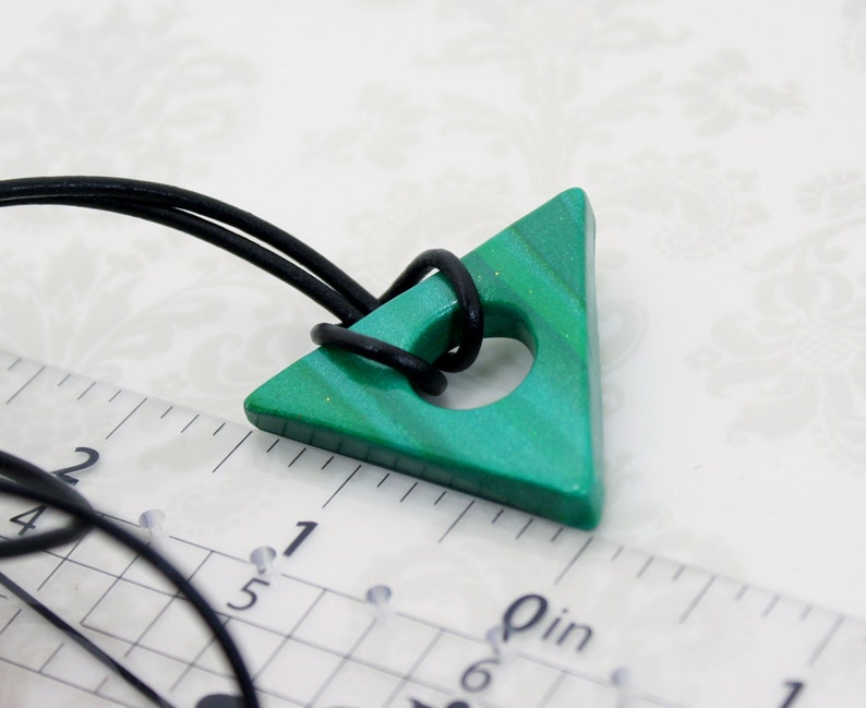 May include: A green triangle pendant with a hole in the center, hanging from a black cord. The pendant is about 1 inch in size and has a marbled pattern.