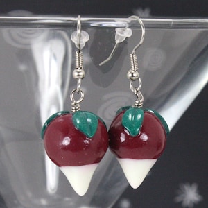 May include: A pair of dangle earrings featuring a red and white beet design with green leaves. The earrings are made of polymer clay and have silver hooks.