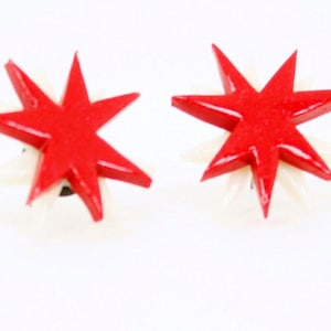 Pu&ograve; includere: Un paio di orecchini a forma di stella rossa con accenti bianchi. Gli orecchini sono realizzati in un materiale lucido e hanno un design semplice e moderno.