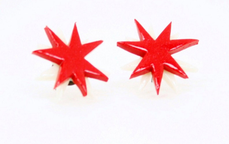 Pu&ograve; includere: Un paio di orecchini a forma di stella rossa con accenti bianchi. Gli orecchini sono realizzati in un materiale lucido e hanno un design semplice e moderno.