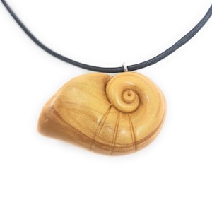 Puede incluir: Un collar con un colgante de concha dorada en un cordón de cuero negro. La concha está detallada con un patrón en espiral y un acabado brillante.