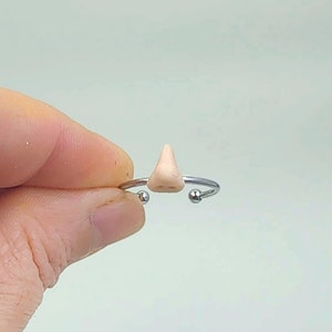 Peut inclure: Une bague en argent avec un petit charme de nez de couleur chair.