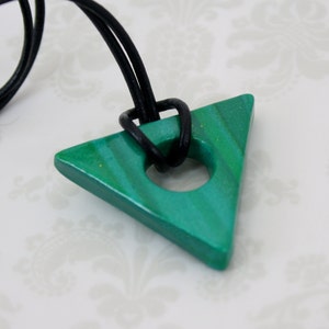 May include: A green triangle pendant with a hole in the center, hanging from a black leather cord. The pendant has a marbled effect and is made of polymer clay.