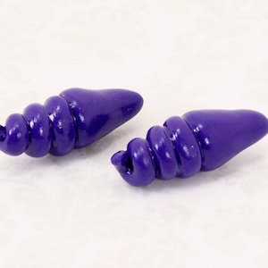 May include: Two deep purple, spiral-shaped beads with a smooth, glossy finish. Each bead features a tapered, conical end and a coiled, shell-like structure, showcasing a vibrant, solid color throughout the entire surface of the objects.