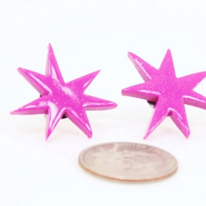 Pu&ograve; includere: Un paio di orecchini a forma di stella rosa con una finitura scintillante. Gli orecchini sono circa delle dimensioni di una moneta da dieci centesimi di euro.