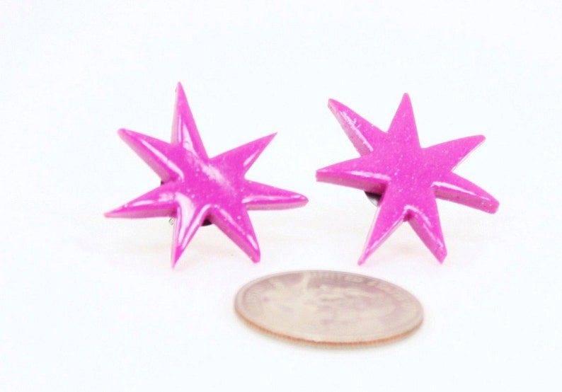 Pu&ograve; includere: Un paio di orecchini a forma di stella rosa con una finitura scintillante. Gli orecchini sono circa delle dimensioni di una moneta da dieci centesimi di euro.