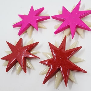 Pu&ograve; includere: Quattro ornamenti decorativi a forma di stella. Due sono rosa con accenti bianchi e due sono rossi con accenti bianchi.
