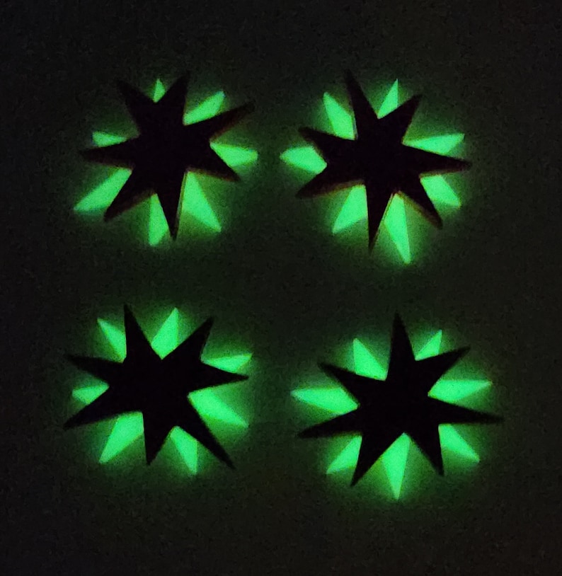 Pu&ograve; includere: Quattro adesivi neri a forma di stella che brillano al buio con bordi verdi. Gli adesivi sono disposti in uno schema quadrato.