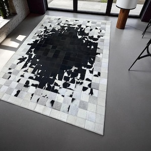 May include: A rectangular area rug with a patchwork design. The rug features a central black section with a mottled pattern, surrounded by a border of white, gray, and black squares. The rug is made of a soft, textured material.