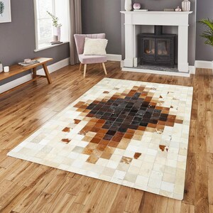 May include: A rectangular rug with a geometric design. The rug has a central diamond pattern in shades of brown and black, set against a cream-colored backdrop. The rug is constructed from squares of material.