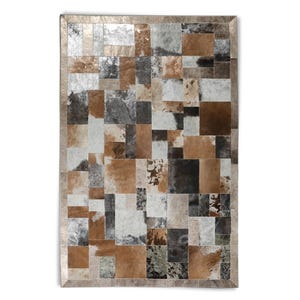 Puede incluir: Una alfombra de patchwork hecha de piel de vaca en tonos marrones, grises y blancos. La alfombra tiene un borde plateado.