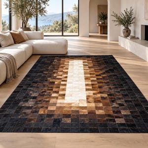 May include: A rectangular area rug featuring a patchwork design of square tiles in varying shades of black, dark brown, tan, and cream. The pattern transitions from dark outer edges to a lighter, cream-coloured central column, creating a gradient effect.