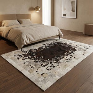 Può includere: Un tappeto rettangolare con un design patchwork. Il tappeto presenta una sezione centrale marrone scuro con un motivo maculato, circondata da un bordo di quadrati più chiari nelle tonalità del bianco, grigio e marrone. Il tappeto è posato su un pavimento in legno.