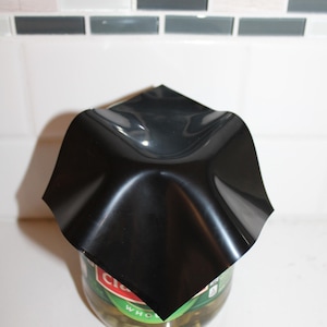 May include: A black plastic food cover is placed over a glass jar of pickles. The jar has a green label with the word "Whole" visible.