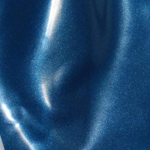 May include: Close-up of a shimmering, deep blue surface with a metallic sheen. The material has subtle folds and highlights, creating a dynamic play of light and shadow. The overall effect is a luxurious, textured appearance.