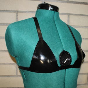 May include: A black, shiny, triangle-shaped bra with thin straps, displayed on a teal dress form. The bra has a horizontal band across the chest and a circular adjustment mechanism in the center.