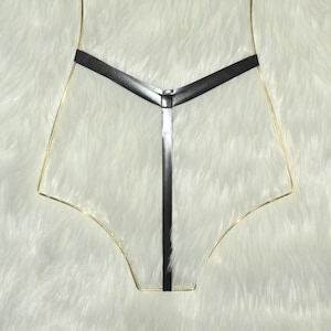May include: Black leather lingerie with a gold wire frame. The lingerie features a V-shaped design across the chest and a vertical strap. The background is a white, fluffy surface.