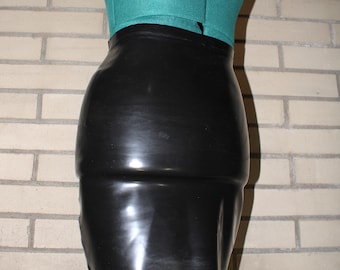 May include: A black, form-fitting skirt made of a shiny material. The skirt is displayed on a mannequin with a teal top. The skirt has a high waist and a smooth, sleek appearance. The background is a brick wall.
