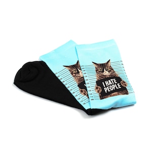 Peut inclure: Paire de chaussettes fantaisie avec un pied noir et une jambe bleu clair. Les chaussettes présentent une illustration de chat avec une pancarte "I HATE PEOPLE" sur un fond d'échelle de taille.