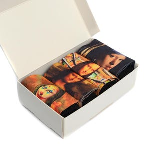 May include: A white box with a set of four pairs of socks. Each sock features a different famous painting, including the Mona Lisa, The Girl with a Pearl Earring, and The Joker.