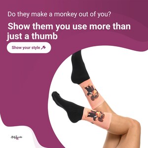 Pode incluir: Um par de meias pretas e cor-de-rosa com um gráfico de um macaco. As meias são mostradas nas pernas de uma pessoa. O texto na imagem diz "Do they make a monkey out of you? Show them you use more than just a thumb. Show your style."