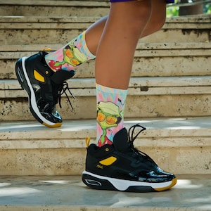 May include: Black and yellow high-top sneakers with a cartoon character on the socks. The socks are white, pink, and blue with a cartoon character wearing sunglasses and a hat.