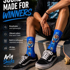 May include: Blue crew socks featuring a graphic print of a soccer player and the Manchester City team logo. The text on the image reads SOCKS MADE FOR WINNERS, Arty Shocks, and step into colors, alongside icons for breathable, vibrant, and washable features.