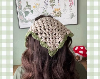 May include: A crocheted headband with a beige and green color scheme. The headband has a scalloped edge and is tied at the back of the head.