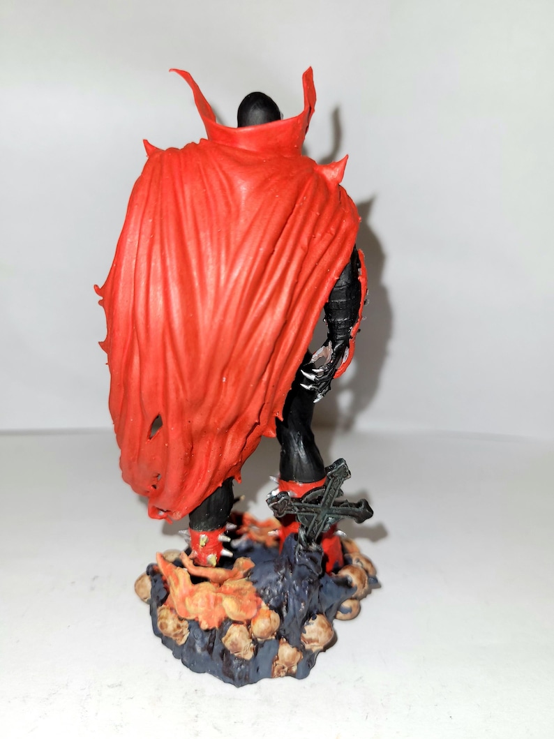 May include: A red and black action figure of a superhero with a cape and a sword. The figure is standing on a base with a skull design.