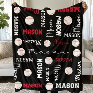 Op de afbeelding: Zwarte fleece deken met honkballen en de naam "Mason" in wit en rood. De naam wordt herhaald in verschillende lettertypen en oriëntaties, waardoor een gepersonaliseerd ontwerp ontstaat.