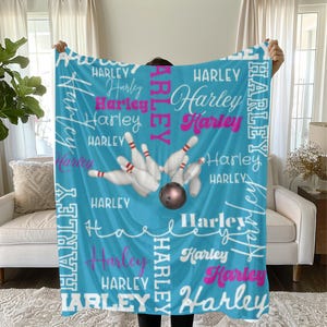 May include: A light blue fleece blanket featuring the name "Harley" in white and pink script. The blanket has a bowling theme, with a bowling ball and pins in the center.