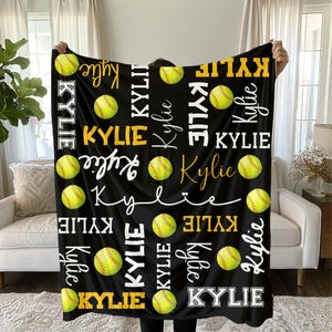 May include: Black softball blanket featuring the name "Kylie" in white and gold lettering, along with yellow softballs. The name is repeated throughout the design in various fonts. A cozy and personalized gift.
